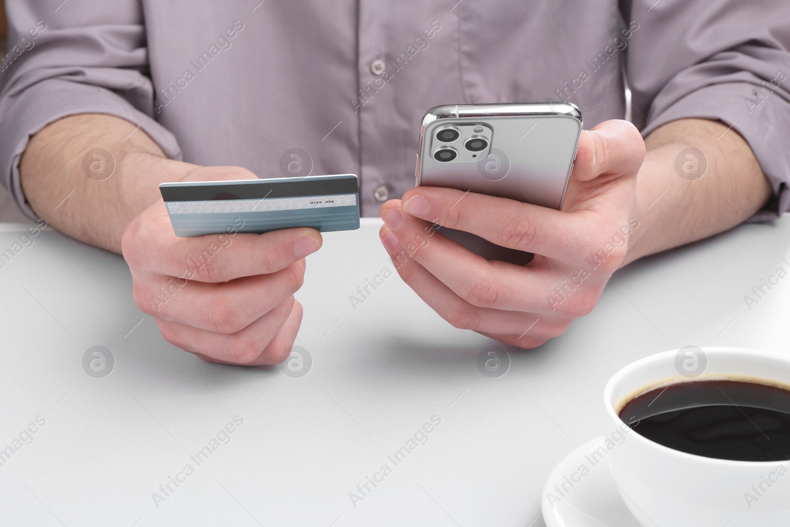 Photo of Online payment. Man with smartphone and credit card at light grey table, closeup