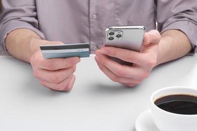 Online payment. Man with smartphone and credit card at light grey table, closeup