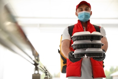 Photo of Courier in protective mask and gloves with order indoors, focus on hands. Restaurant delivery service during coronavirus quarantine