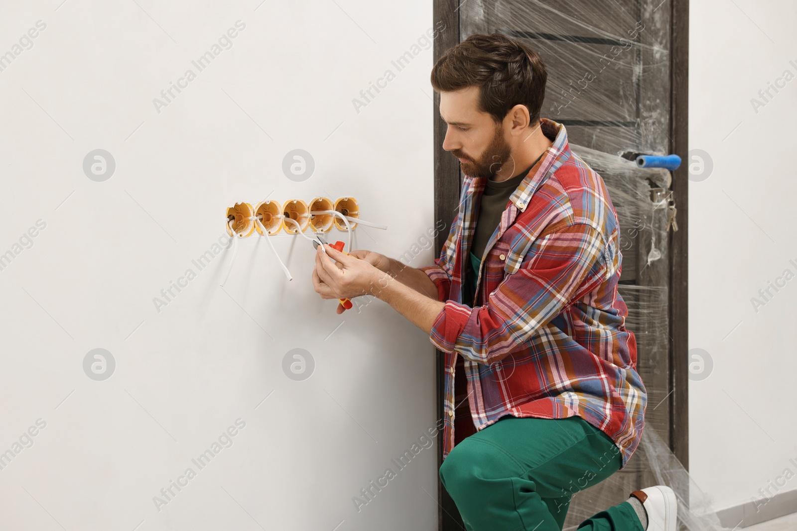 Photo of Professional electrician with pliers fixing wires indoors