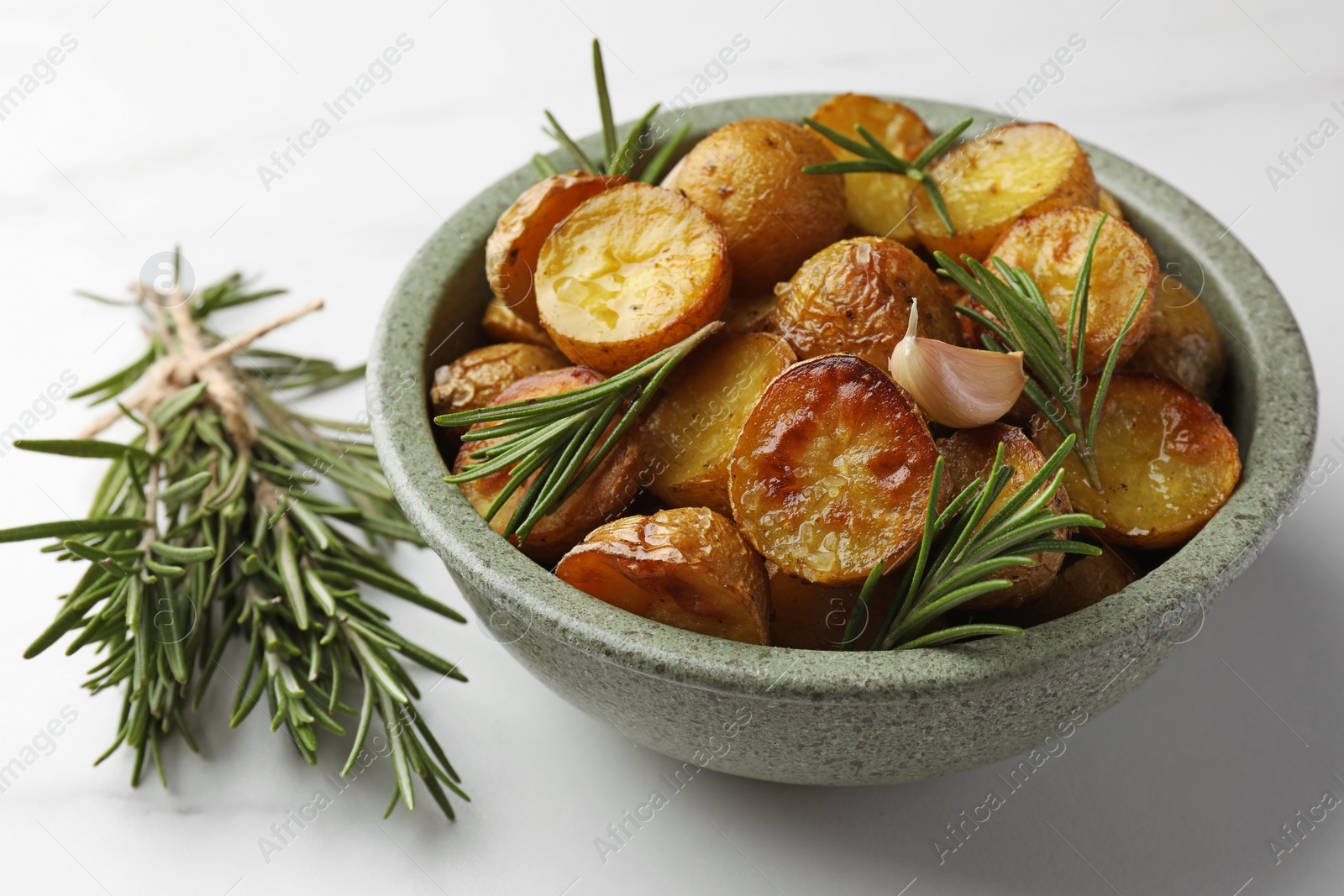 Photo of Bowl with tasty baked potato and aromatic rosemary on white table, closeup