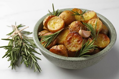 Bowl with tasty baked potato and aromatic rosemary on white table, closeup