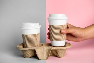 Woman taking paper coffee cup from cardboard holder on color background, closeup