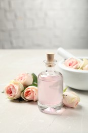 Bottle of rose essential oil and flowers on white table