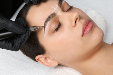 Photo of Beautician making permanent eyebrow makeup to young woman, closeup