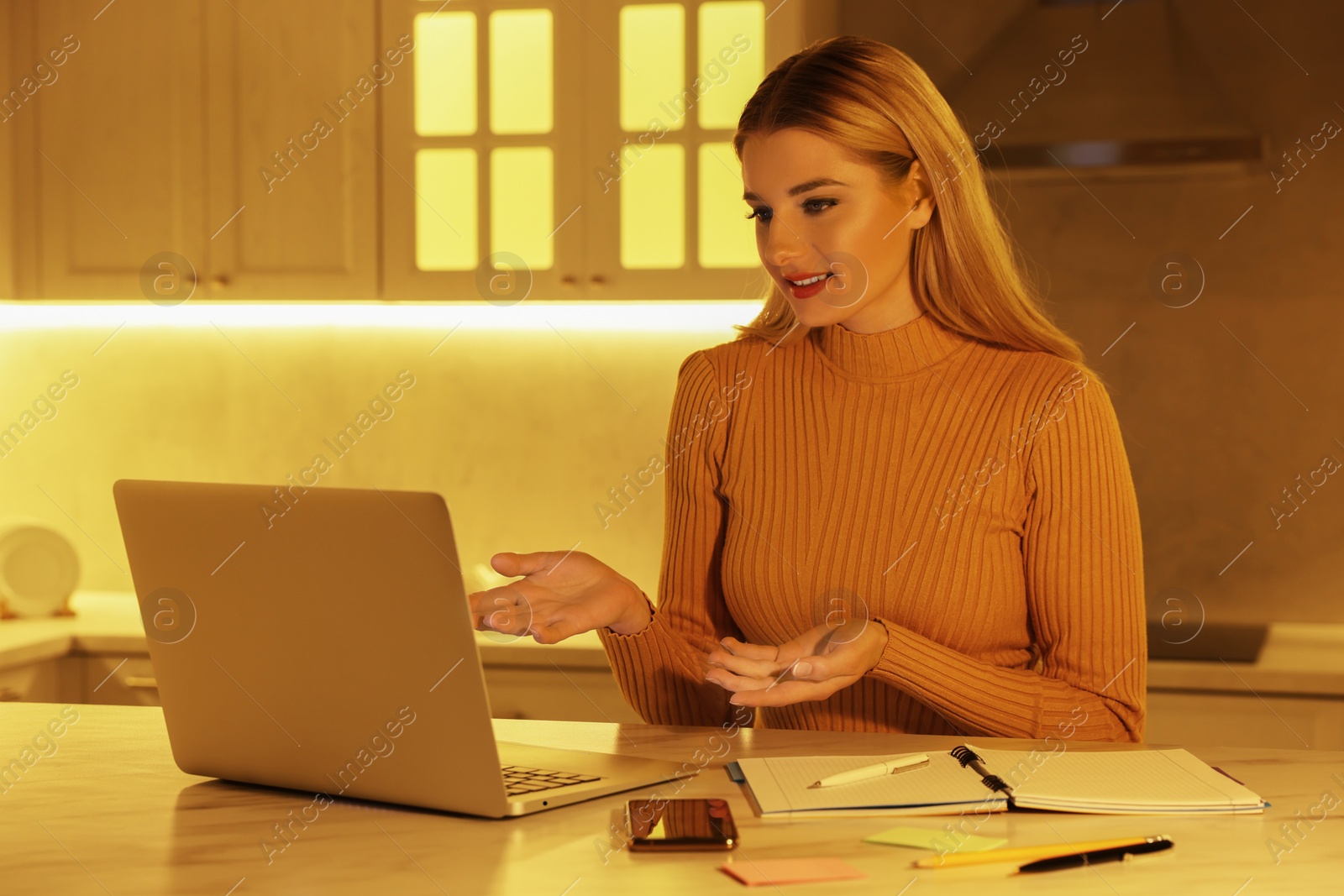 Photo of Home workplace. Woman talking by videochat on laptop at marble desk in kitchen