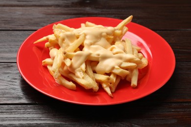 Photo of Delicious french fries with cheese sauce on wooden table, closeup