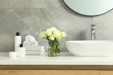 Beautiful roses and bath accessories near sink in bathroom