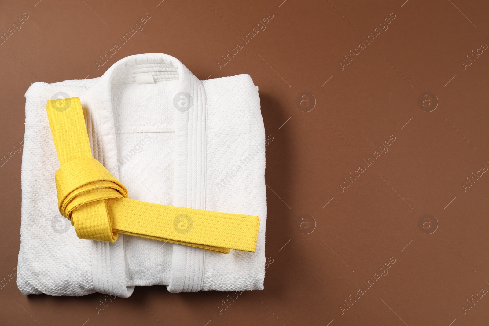 Photo of Yellow karate belt and white kimono on brown background, top view. Space for text