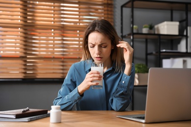 Photo of Woman taking medicine for hangover in office