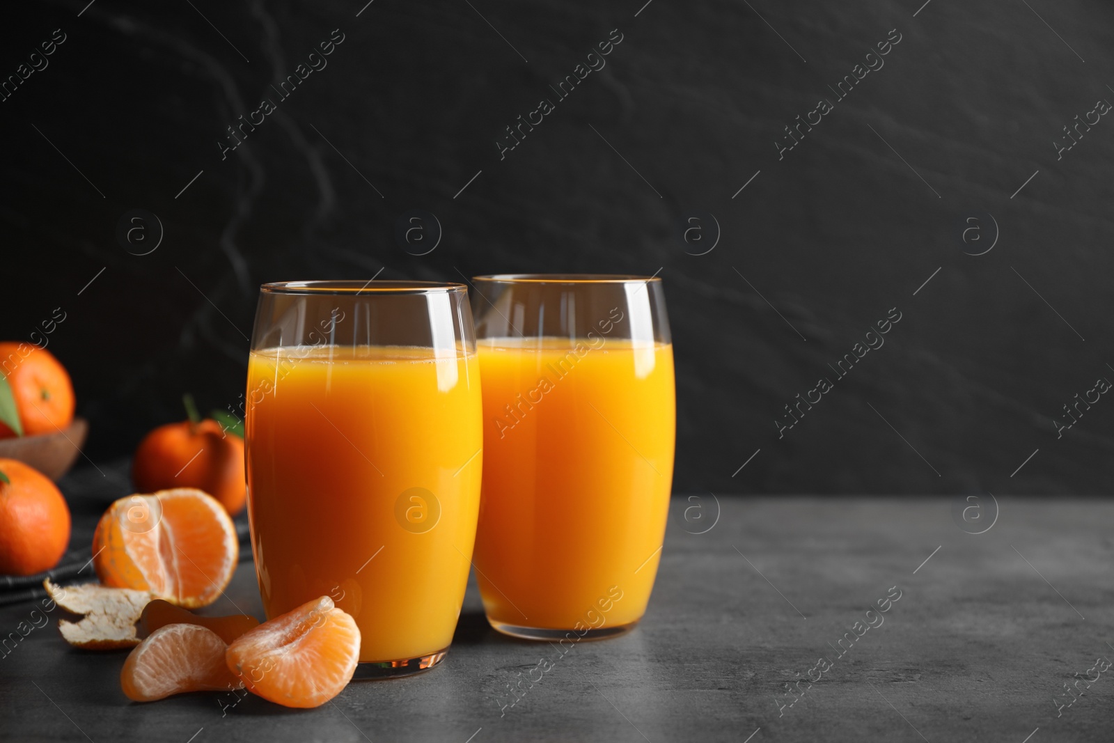 Photo of Fresh tangerines and glasses of juice on grey table