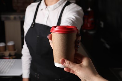 Barista giving takeaway paper cup with coffee to client in cafe, closeup