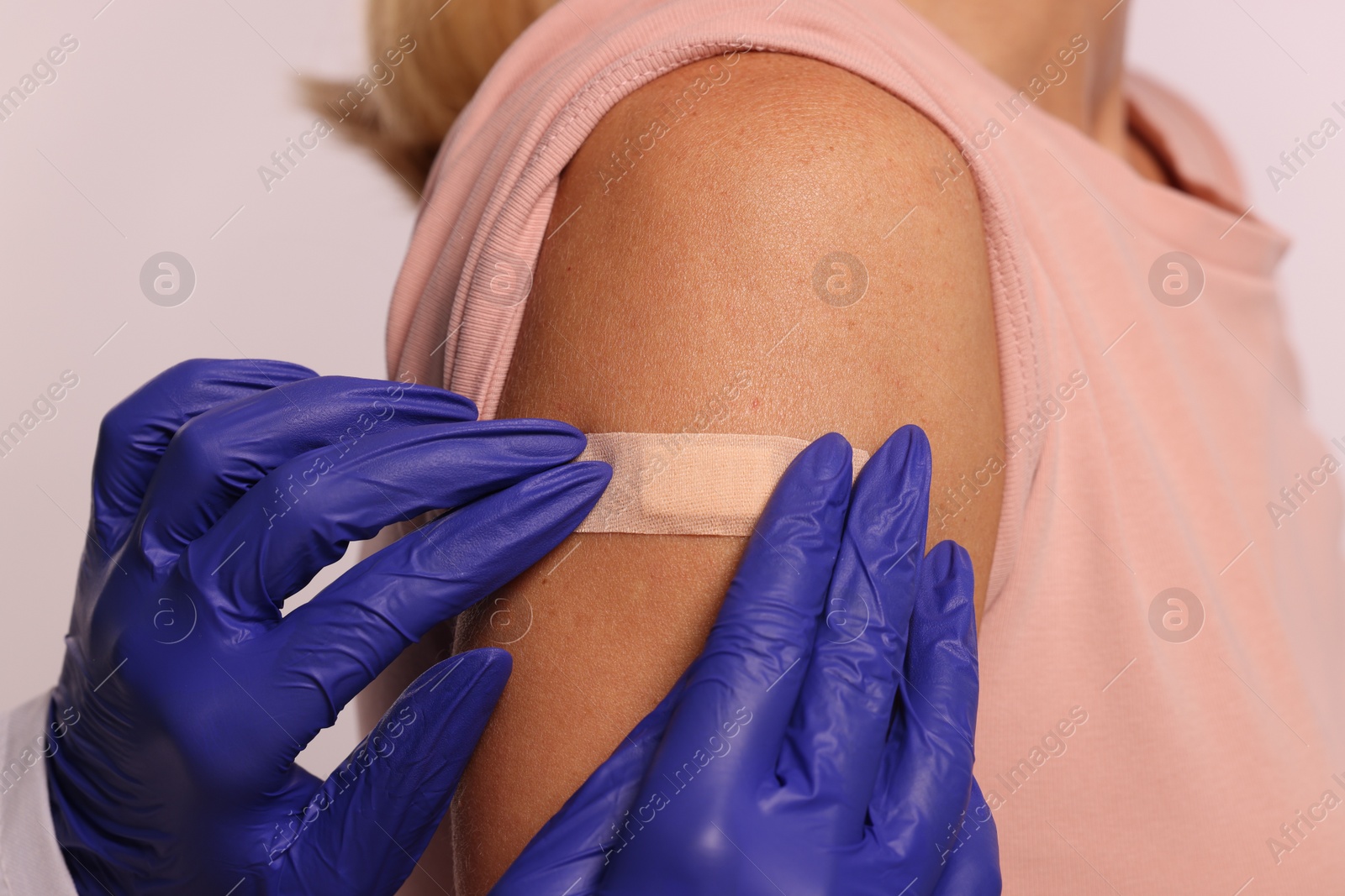 Photo of Nurse sticking adhesive bandage on woman's arm after vaccination on light background, closeup