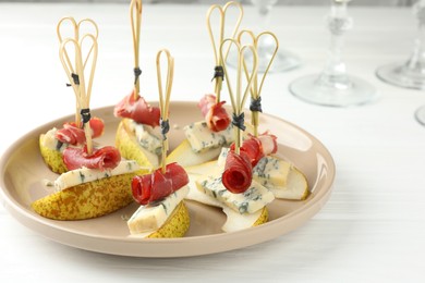 Tasty canapes with pears, blue cheese and prosciutto on white wooden table, closeup