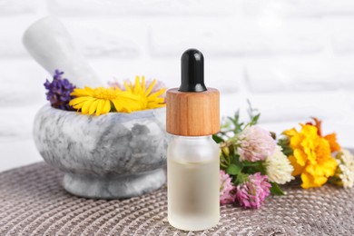 Photo of Glass bottle of essential oil, mortar with pestle and different wildflowers on wicker mat