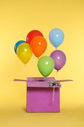 Gift box with bright air balloons on color background