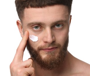Handsome man applying moisturizing cream onto his face on white background