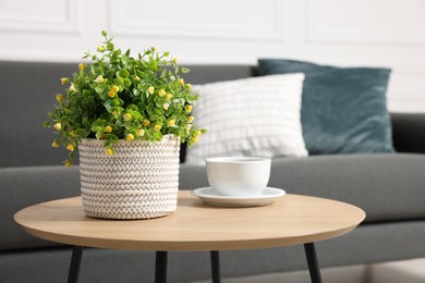 Photo of Potted artificial plant and cup of drink on coffee table near sofa indoors