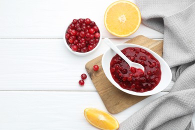 Photo of Tasty cranberry sauce in bowl, fresh berries and orange slices on white wooden table, flat lay. Space for text