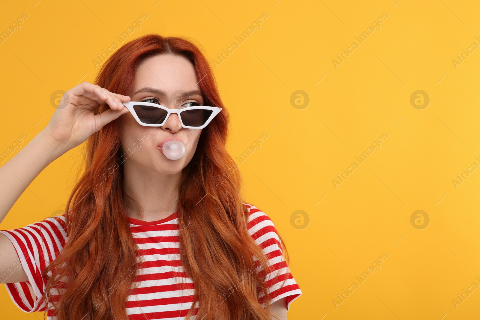 Photo of Beautiful woman in sunglasses blowing bubble gum on orange background. Space for text