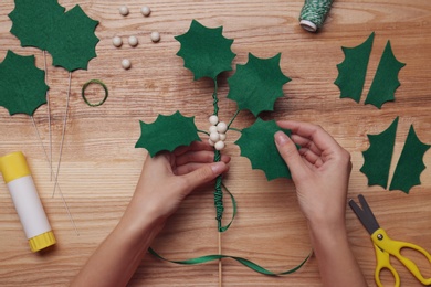 Woman making mistletoe branch at wooden table, top view