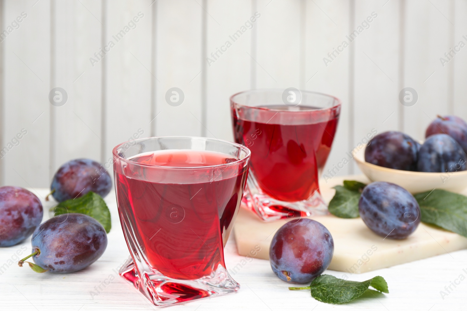 Photo of Delicious plum liquor and ripe fruits on table against white background. Homemade strong alcoholic beverage