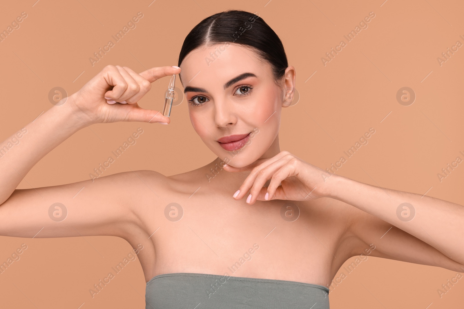 Photo of Beautiful young woman holding skincare ampoule on beige background