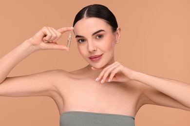 Beautiful young woman holding skincare ampoule on beige background