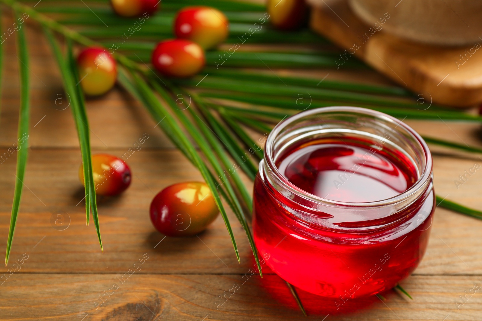 Photo of Palm oil in glass jar, tropical leaf and fruits on wooden table. Space for text