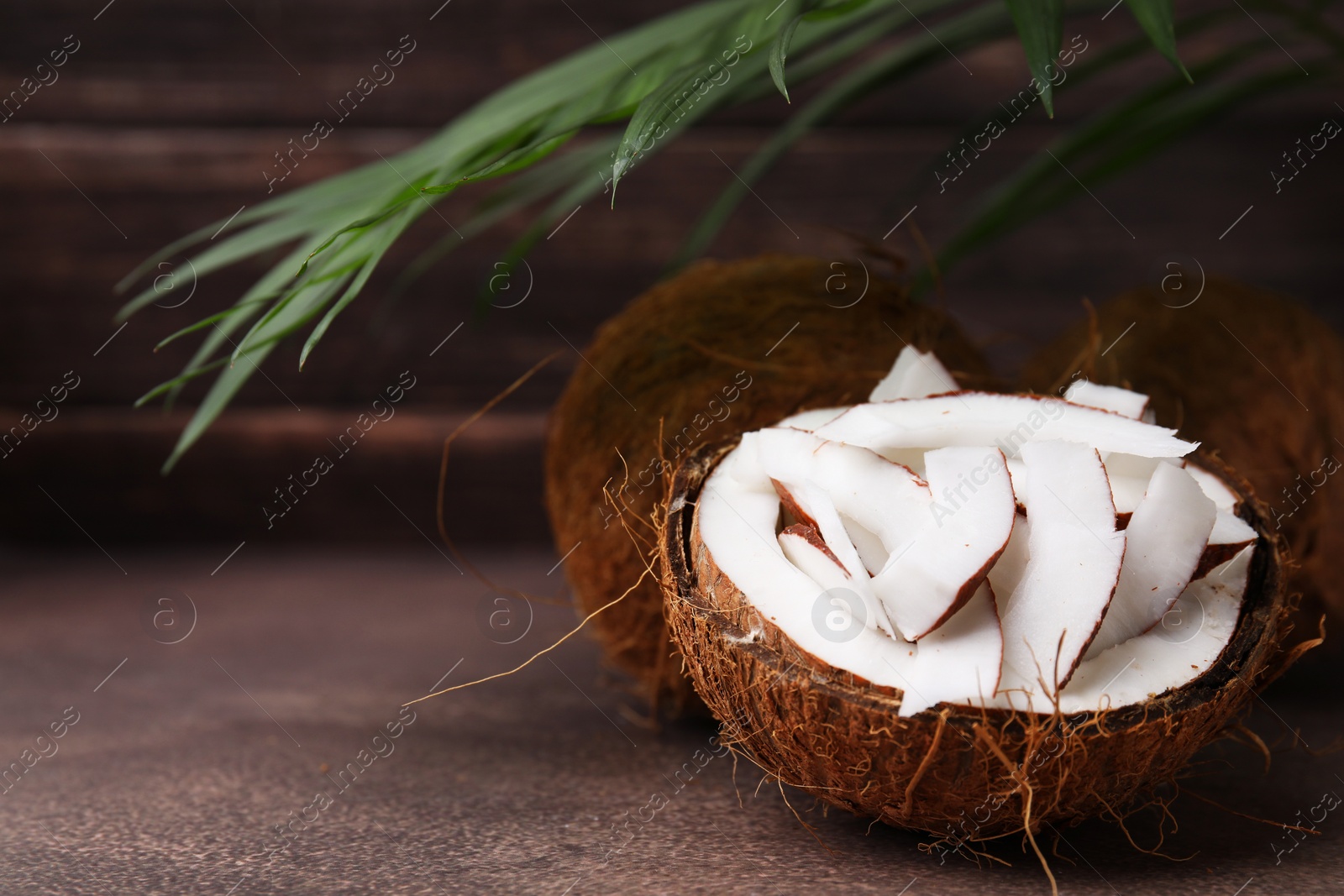 Photo of Coconut pieces in nut shell on brown table, space for text