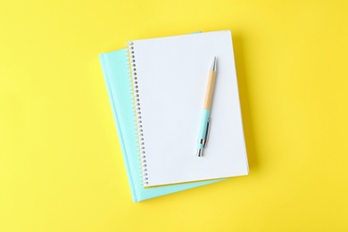 Photo of Notebooks and pen on yellow background, top view