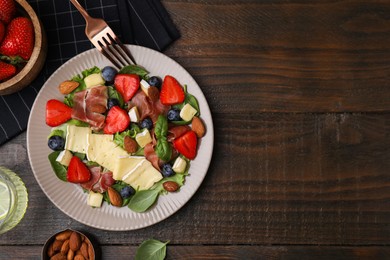 Photo of Tasty salad with brie cheese, prosciutto, almonds and berries served on wooden table, flat lay. Space for text