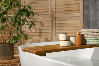 Photo of Wooden tray with spa products and towels on bath tub in bathroom. Space for text