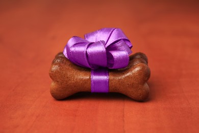 Photo of Bone shaped dog cookies with purple bow on wooden background, closeup