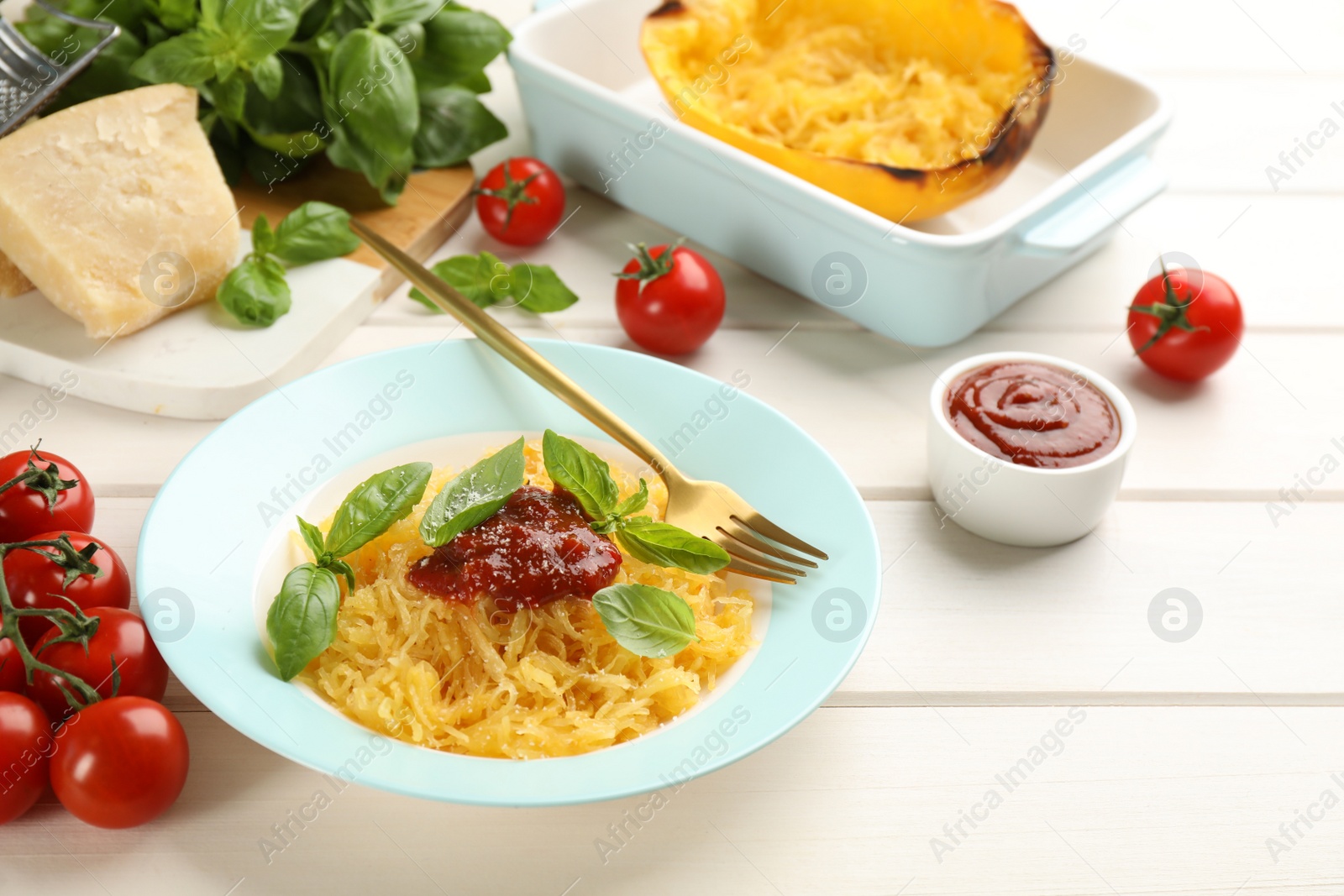 Photo of Tasty spaghetti squash with tomato sauce, cheese and basil served on white wooden table