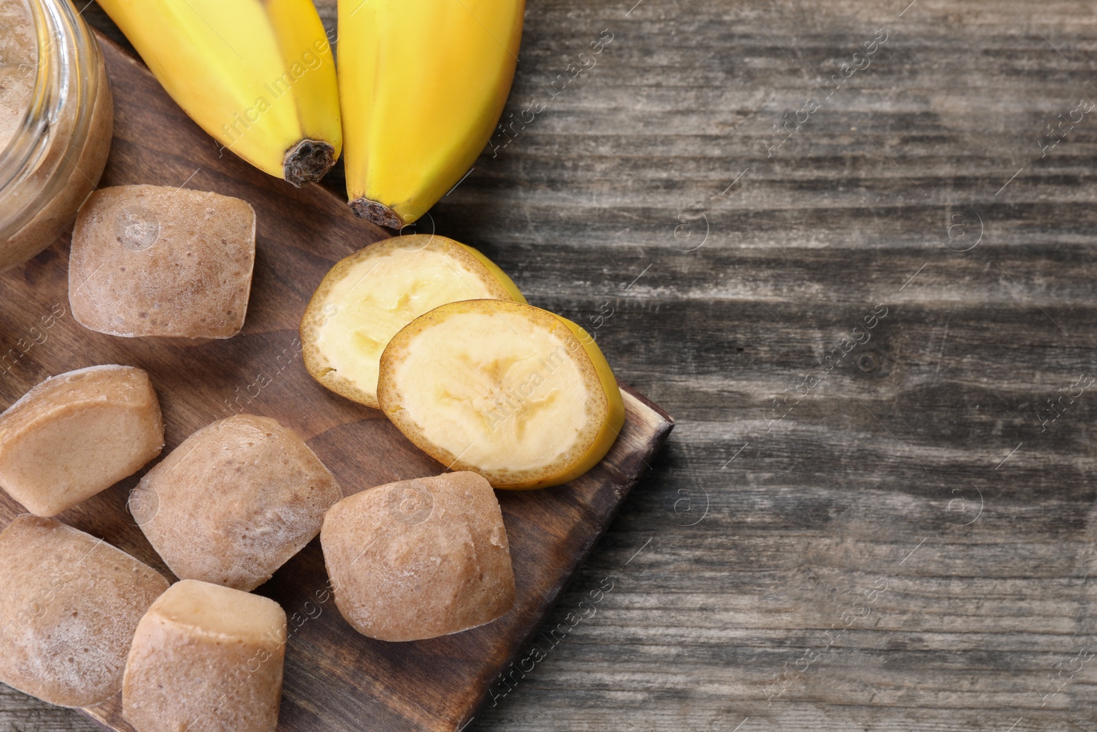 Photo of Frozen banana puree cubes and ingredient on wooden table, flat lay. Space for text