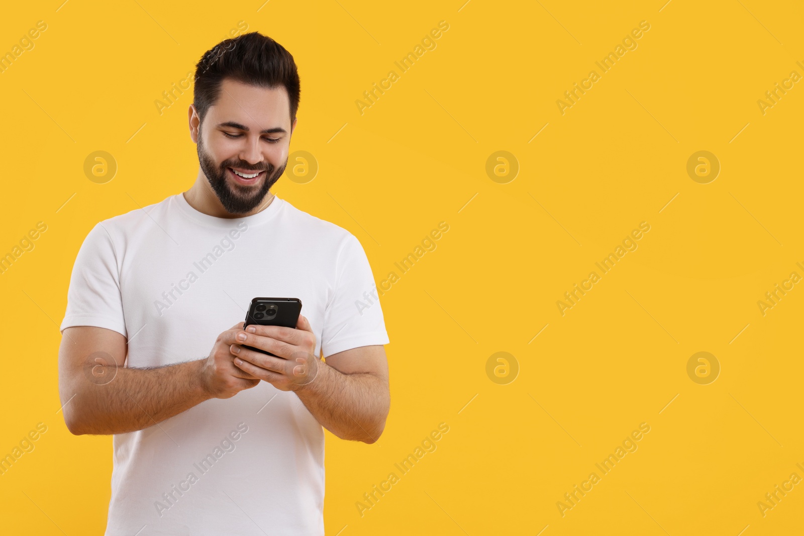 Photo of Happy young man using smartphone on yellow background, space for text