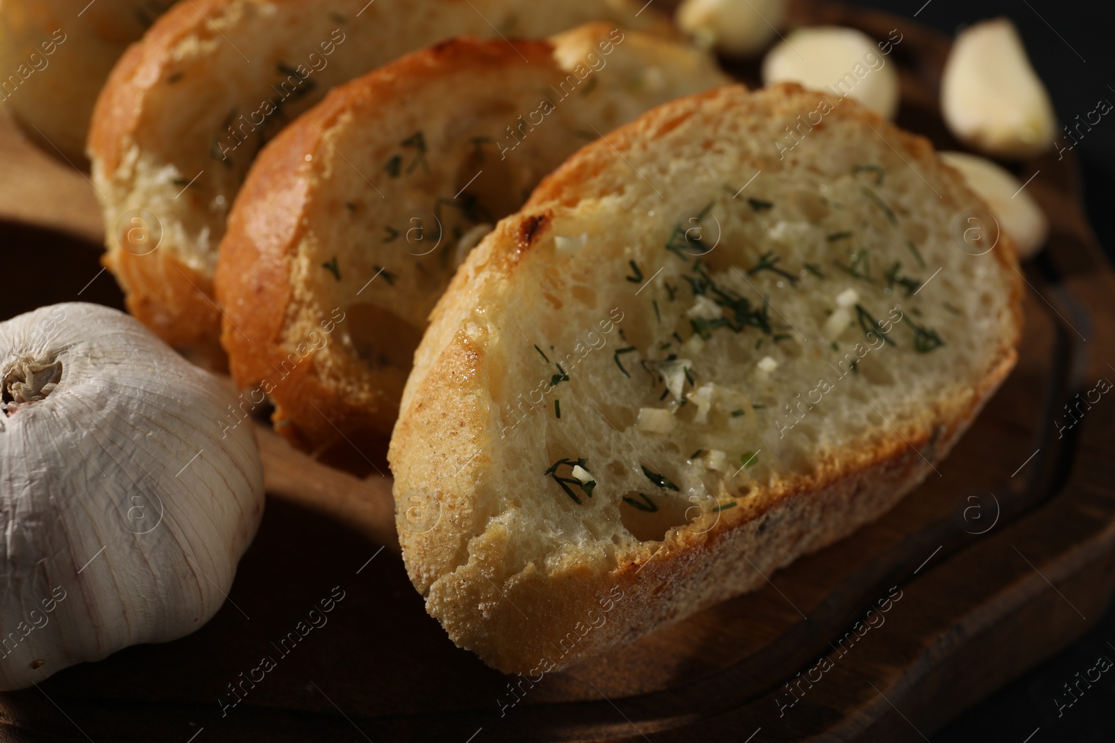 Photo of Tasty baguette with garlic and dill on wooden board, closeup