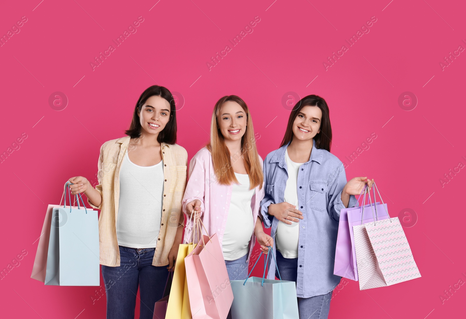 Photo of Happy pregnant women with shopping bags on pink background