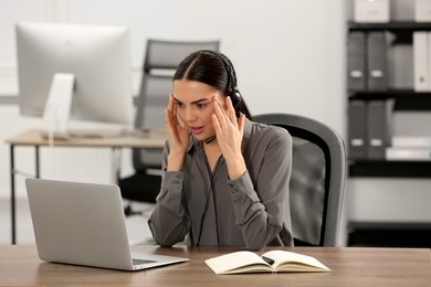 Stressed hotline operator with headset working on laptop in office