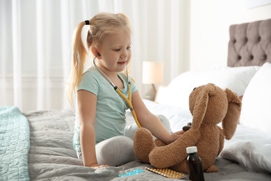 Photo of Cute child imagining herself as doctor while playing with stethoscope and toy bunny at home