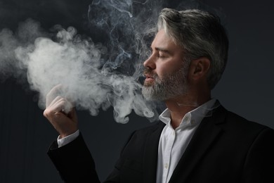 Photo of Handsome bearded man smoking cigar against dark grey background