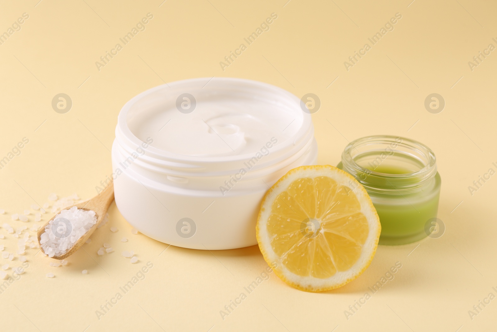 Photo of Moisturizing cream in open jars, sea salt and lemon on beige background. Body care products