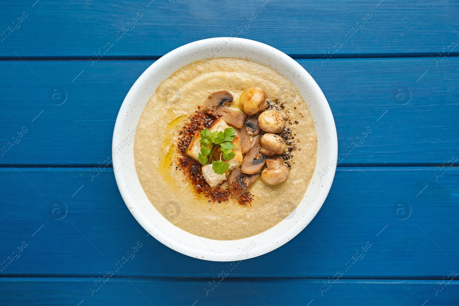 Photo of Delicious cream soup with mushrooms on blue wooden table, top view