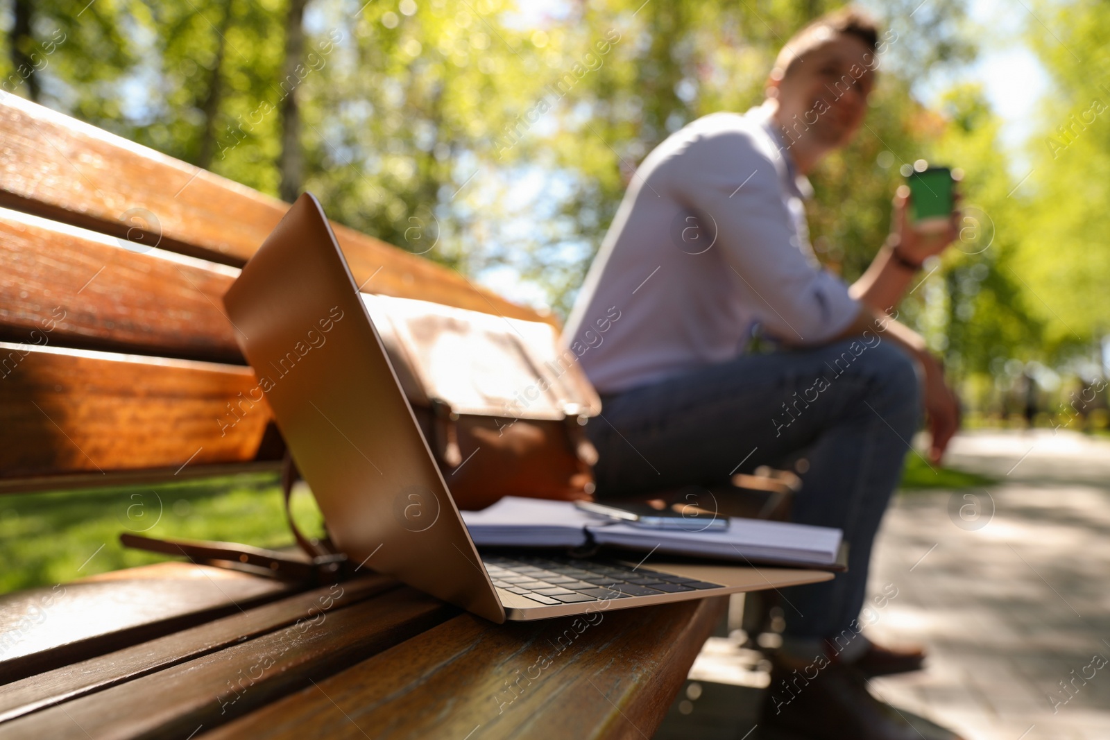 Photo of Man taking coffee break during work in park, focus on laptop