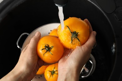 Woman washing fresh ripe yellow tomatoes, closeup