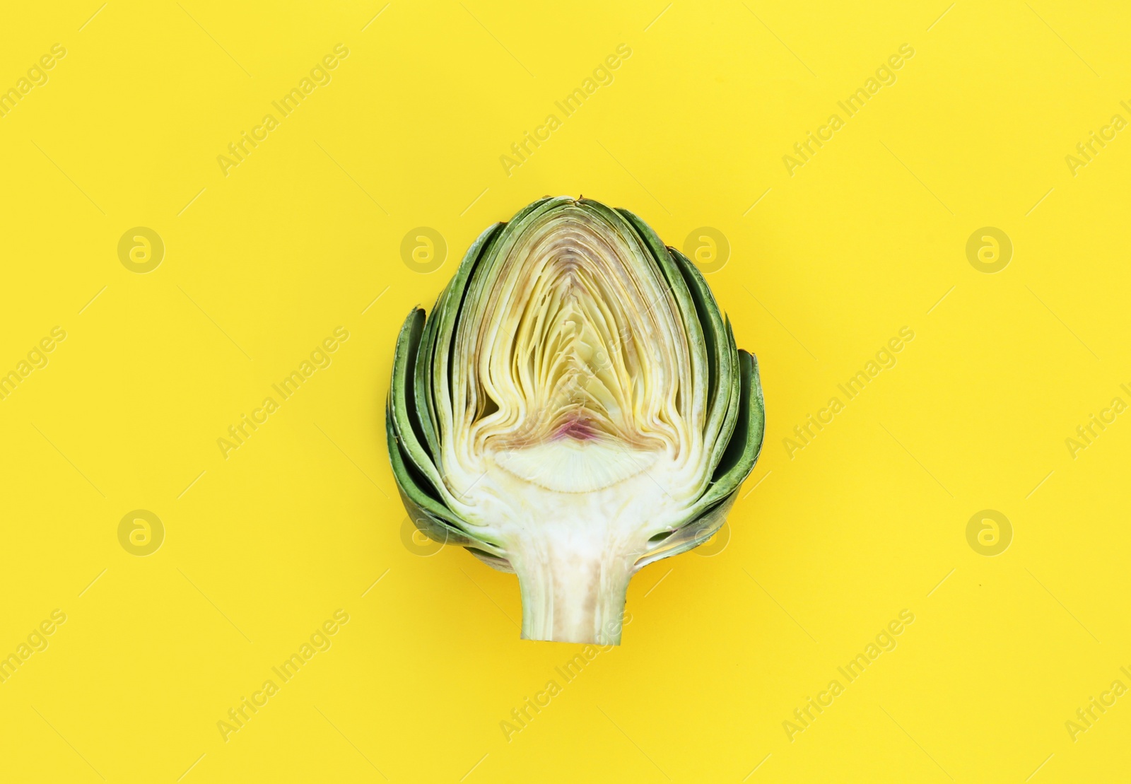 Photo of Half of fresh raw artichoke on pale yellow background, top view