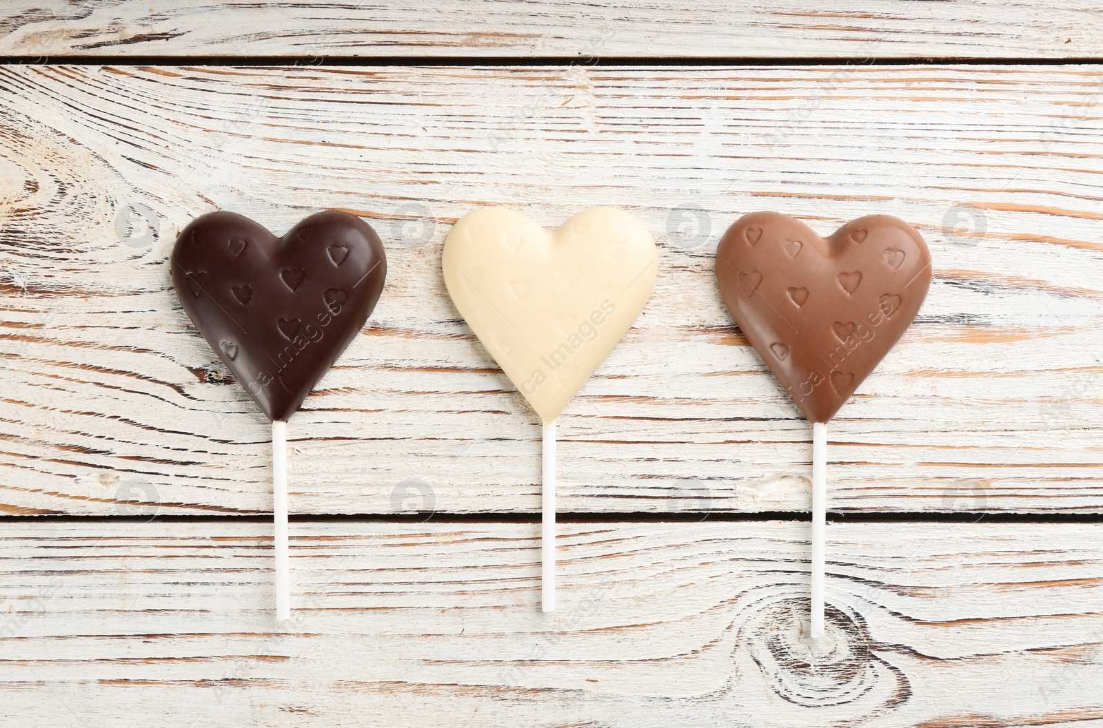 Photo of Different chocolate heart shaped lollipops on white wooden table, flat lay