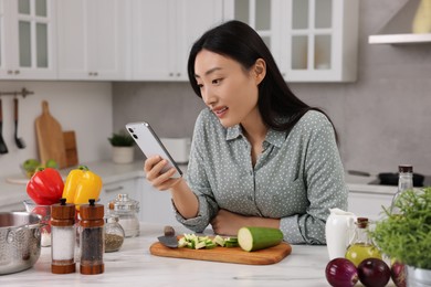 Smiling woman with smartphone cooking in kitchen