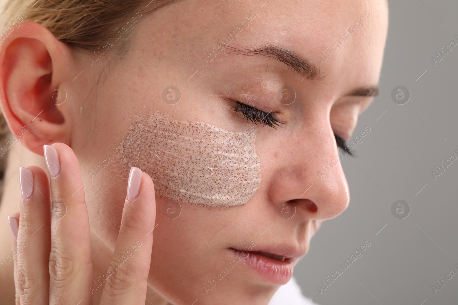 Photo of Woman applying cosmetic product on her face against grey background, closeup. Spa treatments